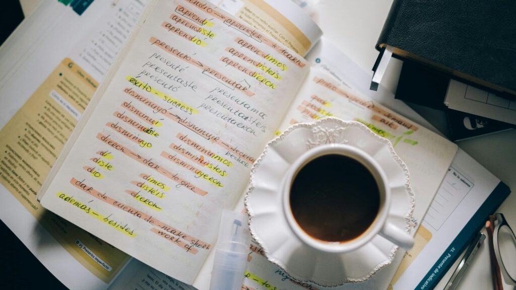 Open notebook on a desk belonging to someone learning Spanish, with Spanish translation and a cup of coffee.