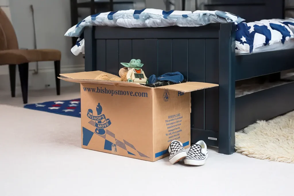A packed Bishop's Move box at the end of a child's bed.