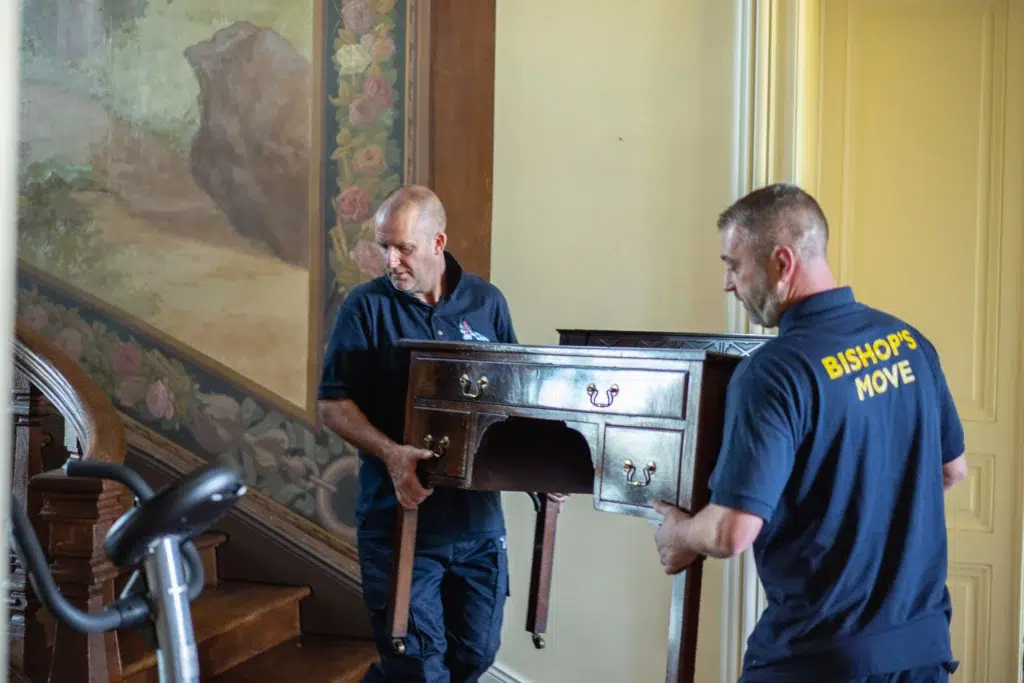 Two removal men carrying an elegant dressing table with drawers down stairs